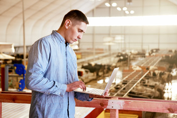 Industrial Automated Farm worker with laptop on the background of the production of cow's milk and beef