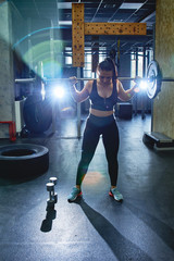 Candid strong young woman is training with a barbell in the gym, doing sit-ups and deadlifts. Real wokout