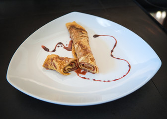 Gefüllter Crepe Pfannkuchen eingerollt und dekoriert auf weißem Teller