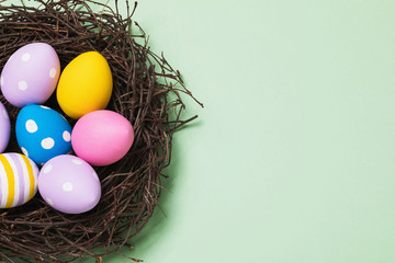 Easter eggs of different colors in a nest on a green background, top view. Festive background with copy space