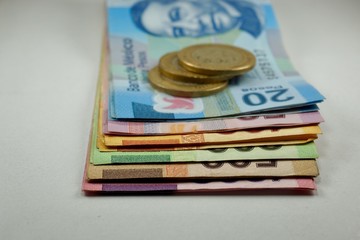 Many mexican pesos bills with coins on top spread over a surface