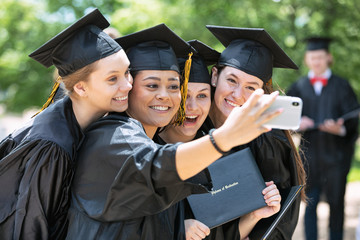 Friends taking selfie with diploma after graduation ceremony on campus