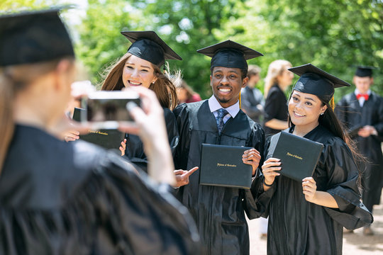 Young woman taking picture of friends with diploma after graduation ceremony on campus
