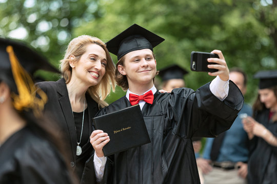 Young man taking selfie along with his mother after graduation ceremony on campus