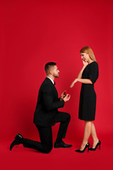 Man with engagement ring making marriage proposal to girlfriend on red background