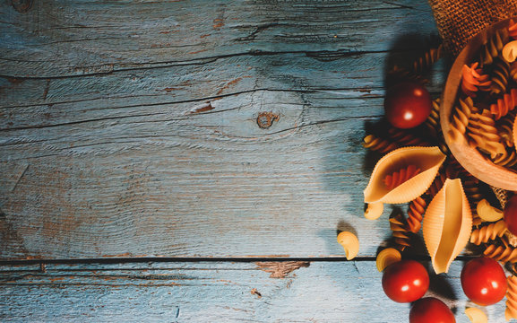 Flat lay composition with different pasta and tomatoes on color background, space for text. Dry uncooked whole pasta