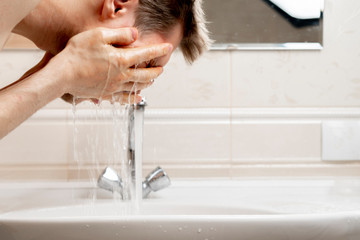 a young bearded man washing his face with splashes in the sink in bathroom, everyday morning routine