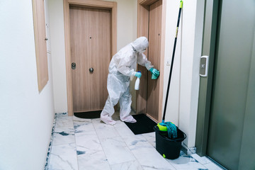 A person protected with safety clothing against a pandemic or virus, cleans and disinfects a portal of a house