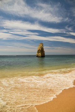 A beautiful composition of waves, clouds and colors in an amazing beach, Praia do Carvalho, Algarve, Portugal. An isolated rock in the ocean.