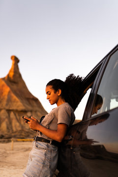Brunette woman lean on the car while she is using the phone, with a castil de tierra peak background.