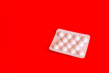 One blister of aspirin tablets on red background with copy space.Anticoagulant medication prescribed to prevent stroke and heart attack.Generic pills.Popular medicine.Painkiller. 