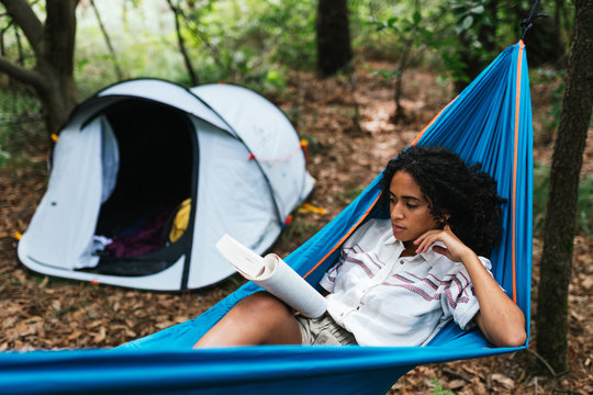 african american woman lying down on a hammock reading a book for camping - Powered by Adobe
