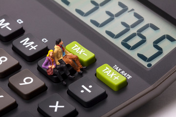 Conceptual image of miniature figure people sat on a calculator next to buttons marked tax