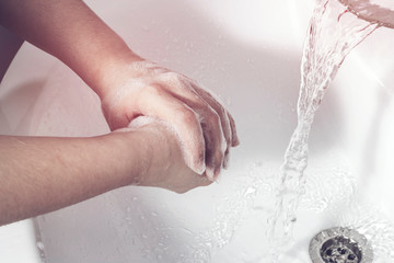Fototapeta premium The girl washes her soapy hands under water from the tap. The concept of protection