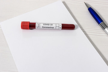 A blood sample in a test tube next to a pen and a white sheet. The concept of the study of coronavirus