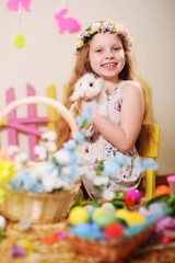 Obraz na płótnie Canvas child-a little girl in a dress and a flower wreath on her head smiling and holding an Easter Bunny on the background of flowers and decor