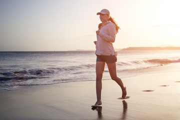Young woman running on ocean beach in the evening