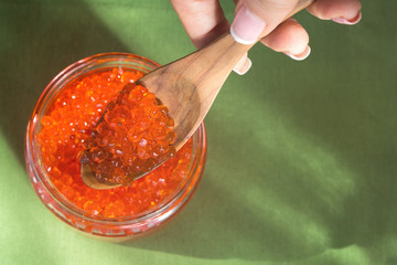 Red vegan caviar from kelp in a glass jar with a wooden spoon on a green background. Valuable and healthy product for a healthy diet. Superfood.