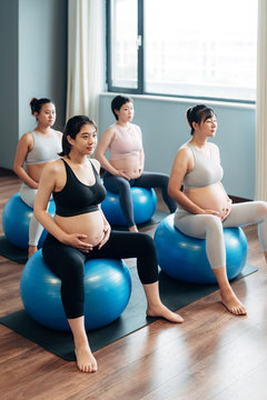 Pregnant women doing yoga exercises and sitting on fitness balls
