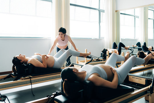 Pregnant woman practicing pilates with equipment reformer