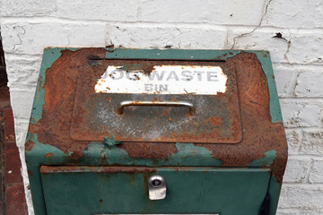 Old Rusty Steel Dog Waste Bin with Shiny Metal Handle Fixed to White Painted Brick Wall 