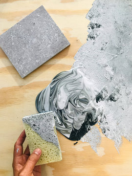Hand holding sponge on grey painted canvas