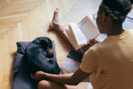 Woman reading a book, spending time with her small black dog ind