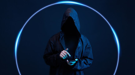 Dangerous hooded hacker with smartphone in his hand. Internet, cyber crime, cyber attack, system breaking and malware concept. Anonymous. Dark background. Black minimalism.