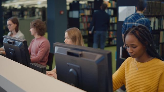 University Library: Diverse Multi-Ethnic Group of Students Work on Computers, Learning, Studying for Exams, Writing Papers, Research Class Assignments, Talk with Classmates. Moving Shot