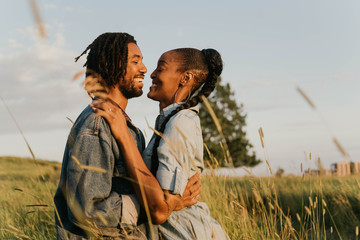 A young engaged African American couple posing for pictures in a field at sunset