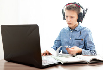  Distance learning in quarantine. A boy in headphones in front of a computer does his homework.