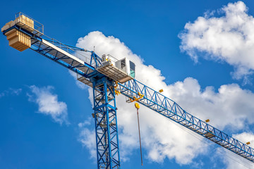 Construction tower crane with a cabin on blue sky with clouds. Bottom view.