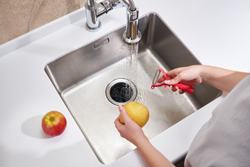 Closeup of woman peeling apple above sink in kitchen