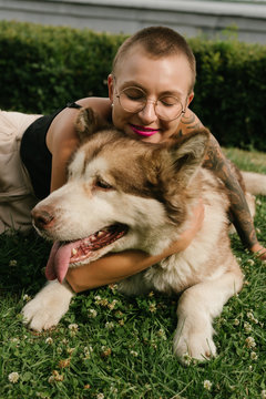 Short-haired girl with the malamut dog sit on the lawn at the park in the sun