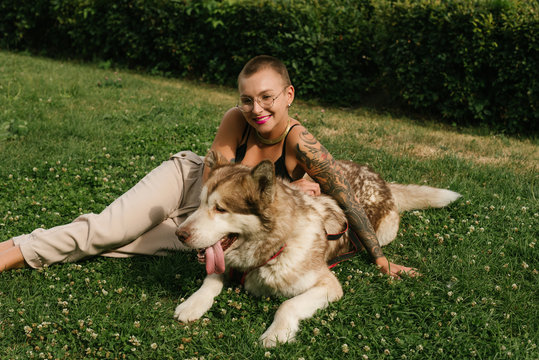 Short-haired girl with the malamut dog sit on the lawn at the park