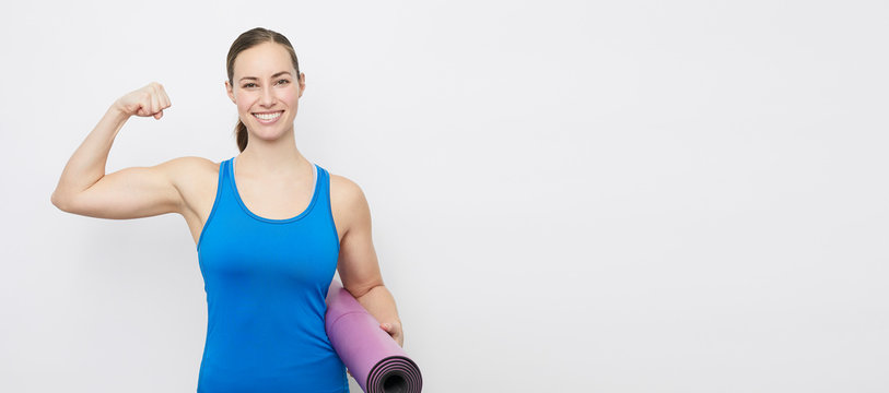 Portrait of young fit and sporty woman showing her strength from her yoga training, stading on a plain backdrop with capyspace 