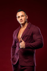 Portrait of handsome stylish man bodybuilder with naked torso in elegant suit. Guy showing thumbs up sign with fingers.