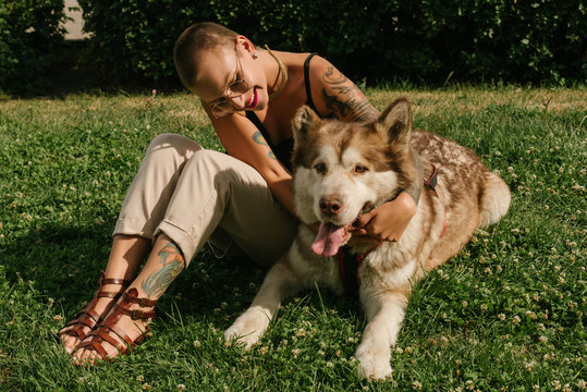 Short-haired girl with the malamut dog sit on the lawn at the park
