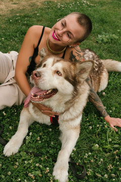 Short-haired girl with the malamut dog sit on the lawn at the park in the sun