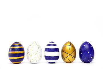 Five easter eggs trendy colored classic blue, white and golden decorated on white table. Happy Easter card with copy space for text. Minimal style.