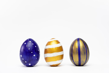 Three easter eggs trendy colored classic blue, white and golden decorated on white table. Happy Easter card with copy space for text. Minimal style.