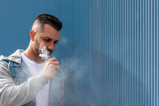 Young man smoking with an electronic cigarette over blue background