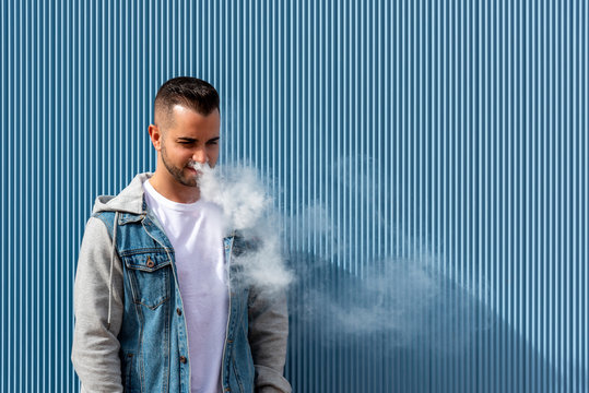 Young man smoking with an electronic cigarette over blue background