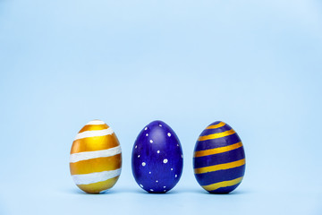 Three easter trendy colored classic blue and golden decorated eggs striped pattern on blue. Happy Easter card with copy space for text. Minimal style.