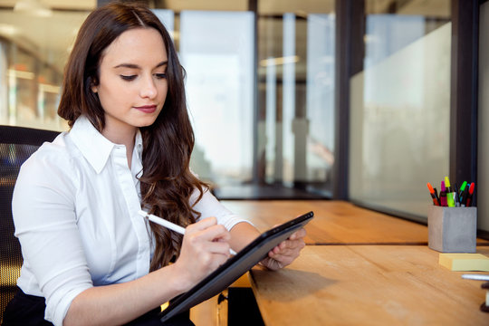 Young business professional at office workspace sitting at desk writing on tablet with electronic stylus pen, writer, journalist, entrepreneur 