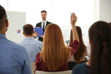 Young woman raising hand to ask question at business training indoors, back view