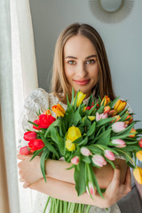 Beautiful young woman holds a multi-colored bouquet of tulips. Spring woman portrait. International Women's Day.