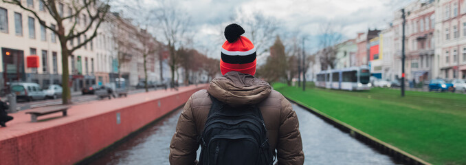 Perspective panoramic banner, back view of young guy, tourist, wearing colorful hat and backpack on...