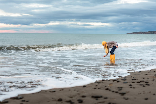 Preteen with yellow boots picking up shell from New Zealand beach