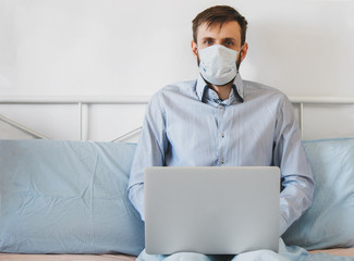 Fototapeta na wymiar young man in medical mask and shirt works from home in his bed with a laptop 